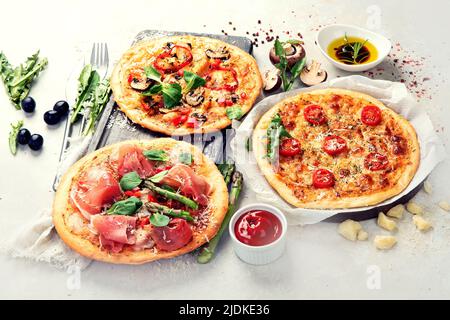 Verschiedene Arten von italienischer Pizza - Margherita, Pepperoni, Schinken, Pilze mit Basilikum, Tomaten, Olivenöl und Käse auf weißem Hintergrund. Draufsicht. Stockfoto