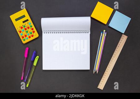 Notizblock, gelber Taschenrechner, Stifte und Stifte, Aufkleber, Lineal auf schwarzem Hintergrund. Schreibwaren für Business, Studium. Konzept zurück zur Schule, Finanzen. Stockfoto