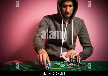 Unglücklicher junger Mann, der sich traurig, verzweifelt und gestresst fühlt, nachdem er sein Geld beim Poker und Blackjack in einem nächtlichen Casino verloren hat Stockfoto
