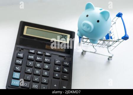 Stillleben beim Einkaufen. Einkaufswagen, Sparschwein, Taschenrechner Stockfoto