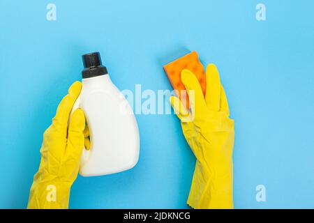 Die Hände einer Hausfrau in gelben Gummischutzhandschuhen halten eine Flasche Haushaltschemikalien und einen Lappen. Reinigungsmittel für verschiedene Oberflächen im Kitc Stockfoto