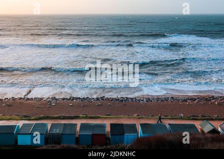 Boscombe in der Nähe von Bournemouth im Winter mit kleinen Strandhütten und Leuten, die am Strand spazieren Stockfoto