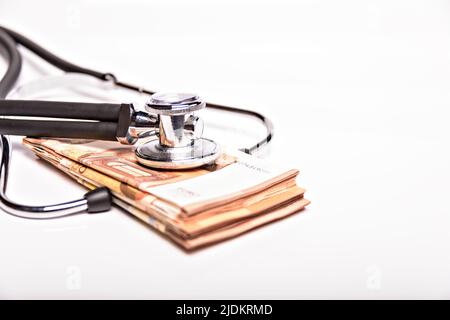 Gesundheitskosten konzeptionelles Bild: Stethoskop und Geldhaufen auf einer medizinischen Karte, Symbol der Gesundheitskosten oder Krankenversicherung, isoliert auf Stockfoto