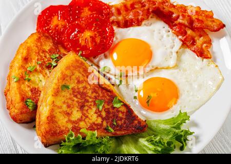 Spiegeleier, Raser- oder Speckscheiben, Kartoffelfarne, gegrillte Tomaten und frischer Salat auf weißem Teller auf weißem Holztisch, irisches Frühstück, Nahaufnahme Stockfoto