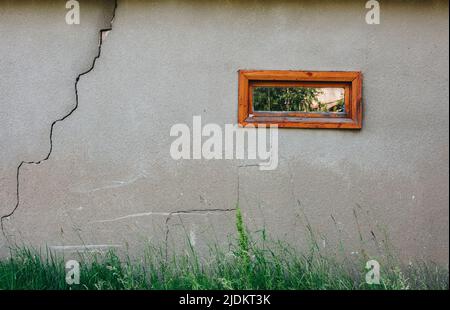 Schöne, graue Betonhauswand mit Fragmenten und einem kleinen Kasten mit einem orangefarbenen Holzrahmen, der schöne grüne Sommerbäume widerspiegelt. Stockfoto