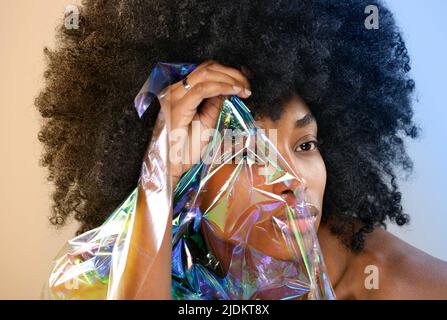 Porträt einer schönen schwarzen Frau mit einem halben Gesicht, das in einem dünnen Plastikfilm in einer Nahaufnahme eingeschlossen ist Stockfoto