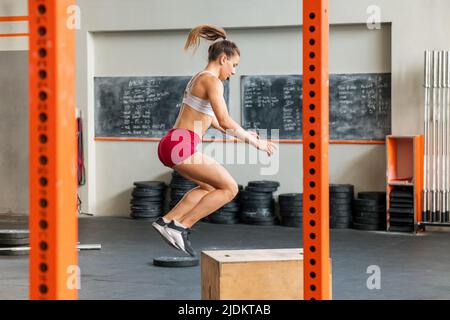 Atletic junge Frau macht eine Crossfit Box Sprung Übung in einem Fitnessstudio in einem Gesundheits-und Fitness-Konzept Stockfoto