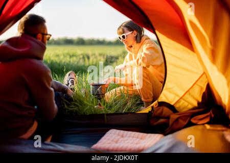 Paar bereiten Essen zu, während sie mit Zelt auf der Natur reisen Stockfoto