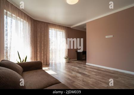 Großes, geräumiges Zimmer oder Wohnzimmer mit Sofa und großen Fenstern in minimalistischem Stil und Pastellfarben. Stockfoto