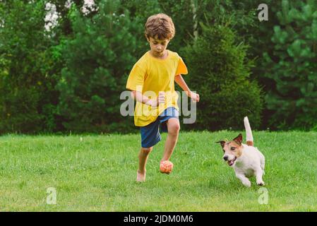 Boy will Fußballspieler sein nutzt Heimtierspielzeug anstelle von Fußball, um mit seinem Hund zu trainieren und Fußball zu spielen Stockfoto