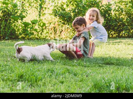 Glücklich lächelnde Kinder spielen Tauziehen Spiel mit ihrem sturen Hund Stockfoto