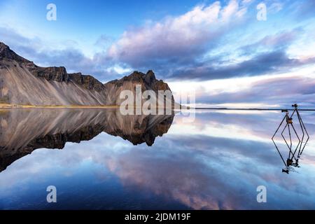 Die Berge von Vestrahorn spiegeln sich in flachen Gewässern im Süden Islands wider. Zwei Stative sind so eingestellt, dass sie diese perfekte Spiegelreflexion fotografieren können. Stockfoto