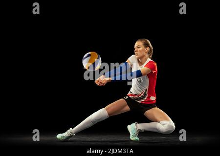 Dynamisches Porträt eines professionellen Volleyballspielers in Sportuniform, der Volleyball auf dunklem Hintergrund spielt. Sport, gesunder Lebensstil, Team Stockfoto