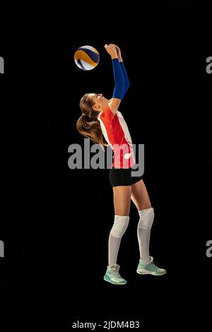 Dynamisches Porträt eines professionellen Volleyballspielers in Sportuniform, der Volleyball auf dunklem Hintergrund spielt. Sport, gesunder Lebensstil, Team Stockfoto