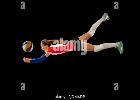 Dynamisches Porträt eines professionellen Volleyballspielers in Sportuniform, der Volleyball auf dunklem Hintergrund spielt. Sport, gesunder Lebensstil, Team Stockfoto