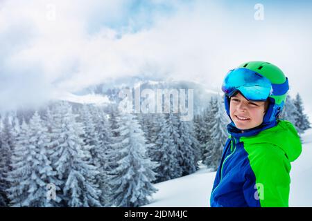 Junge in Skihelm und Maske lächeln über Wald stehen Stockfoto