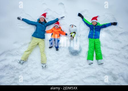 Familie im Schnee zusammen mit Schneemann tragen Weihnachtsmützen Draufsicht Stockfoto