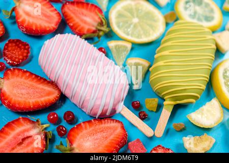 Zwei Eiscremes auf einem Stock - Erdbeere und Zitrone auf blauem Hintergrund. Sommerliche Fruchtdesserts Stockfoto