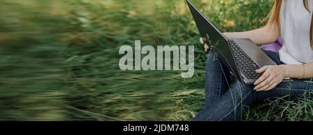 Auf dem Banner arbeitet ein junges Mädchen mit einem Laptop an der frischen Luft im Park und sitzt auf dem Rasen. Das Konzept der Fernarbeit. Arbeiten Sie als Freiberufler. T Stockfoto