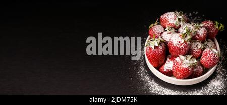 Erdbeeren auf einem Teller mit Puderzucker auf schwarzem Hintergrund, Nahaufnahme, langes Banner. Stockfoto