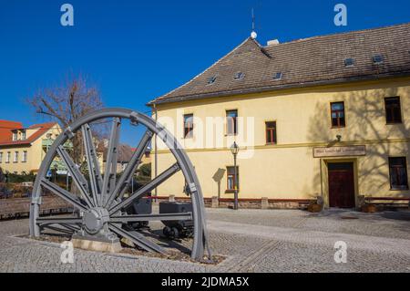 Industrierad und Kohlewagen vor einem historischen Gebäude in Eisleben, Deutschland Stockfoto