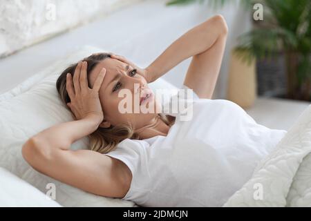 Gestresste Frau, die an Schlaflosigkeit leidet und ihren Kopf berührt Stockfoto