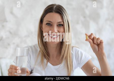 Schöne blonde Dame mit Pille und Glas Wasser Stockfoto