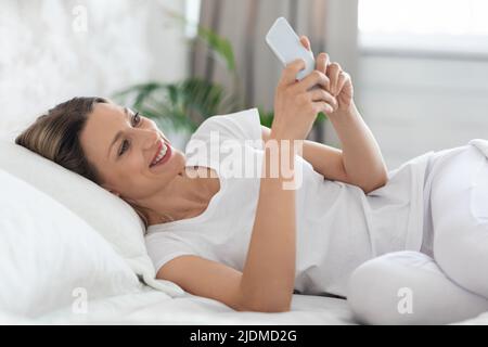 Glückliche blonde Dame im Chat mit Freunden, mit dem Handy Stockfoto