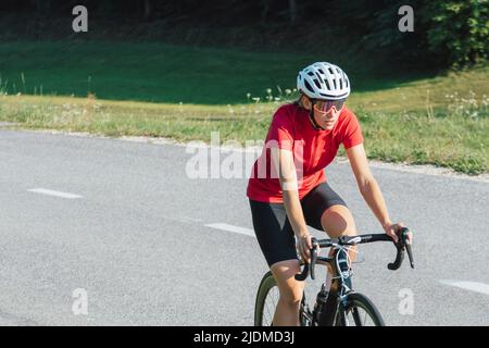 Junge professionelle Radfahrerin während des Rennradsprints, kontinuierliche Bewegung mit maximaler Anstrengung, Nahaufnahme. Stockfoto