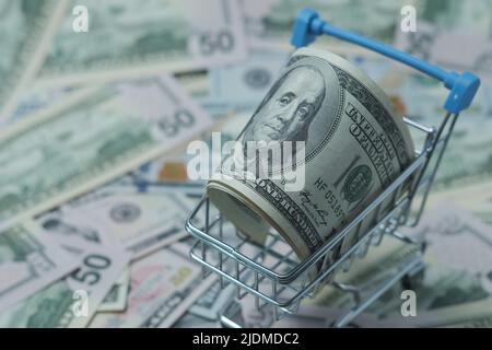 In einen Schlauch gerollte Dollars liegen in einem Einkaufskorb. Der Korb steht auf einem verschwommenen Geldhintergrund. Stockfoto