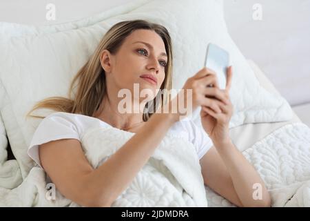 Schöne Frau, die mit dem Smartphone im Bett lag Stockfoto