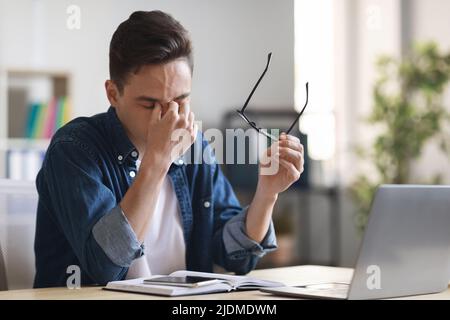 Mitarbeiter Im Millenial Office, Der Nach Der Arbeit Mit Dem Laptop Am Schreibtisch Die Augen Reibt, Müde Stockfoto