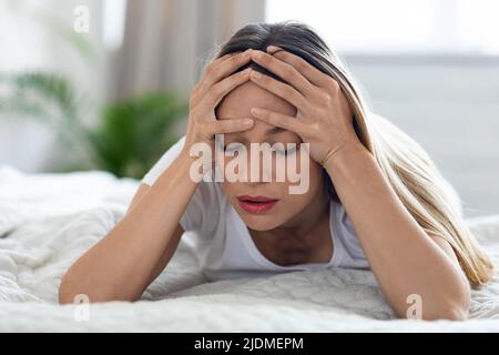 Unglückliche blonde Frau, die an Migräne leidet, häusliche Einrichtung Stockfoto