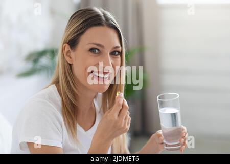 Lächelnde hübsche Frau, die nach dem Aufwachen die Pille nahm Stockfoto