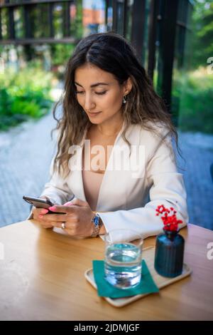 Junge Brünette Geschäftsfrau mit Smartphone SMS und Nachrichten im Straßencafe von Prag lesen Stockfoto