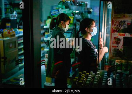 Hongkong, China. 21.. Juni 2022. Zwei weibliche Angestellte arrangieren Produkte in einem Geschäft, während sie ihre Telefone zum Leuchten benutzen. 140.000 Haushalte in Hongkong stehen nach einem Stromkabelbrand vor einem Stromausfall. Kredit: SOPA Images Limited/Alamy Live Nachrichten Stockfoto