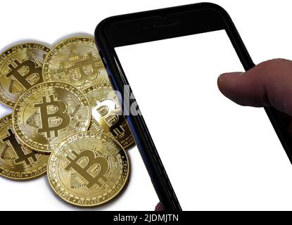 Bitcoin-Münzen aus goldenem Metall mit einer Männerhand neben ihm und einem Smartphone Stockfoto