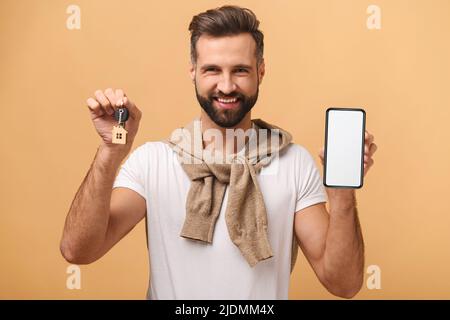 Man hält Smartphone mit leerem Bildschirm und Tasten mit Schlüsselbund in Hausform. Happy Guy zeigt neue App für die Vermietung von Immobilien, Online-Plattform für den Kauf und Verkauf von Immobilien Stockfoto