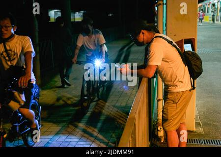 Hongkong, China. 21.. Juni 2022. Ein Mann schaut auf sein Smartphone, während zwei Männer am Light Train Station in Tin Shui Wai vorbeifahren. 140.000 Haushalte in Hongkong stehen nach einem Stromkabelbrand vor einem Stromausfall. (Foto von Emmanuel Serna/ SOPA Images/Sipa USA) Quelle: SIPA USA/Alamy Live News Stockfoto