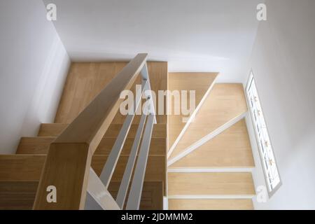 Die moderne geschwungene Holztreppe mit dem weißen Metallgeländer im Stadthaus, sauber und hygienisch vom Haushälter, oben mit der Kopie Stockfoto