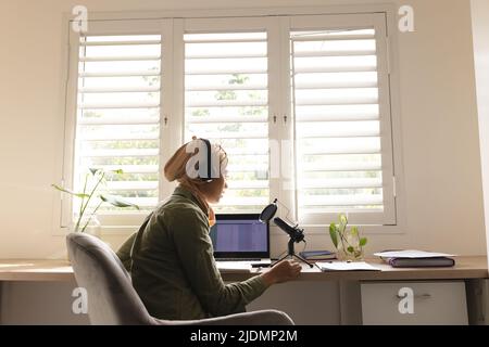 Biracial junge Frau in Hijab Aufnahme Podcast durch Kondensatormikrofon zu Hause Studio Stockfoto