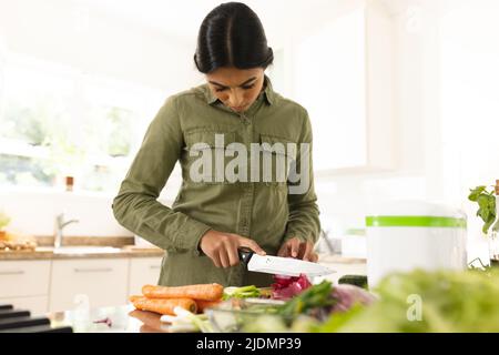 Biracial junge Frau hackt Gemüse auf Schneidebrett in der Küche zu Hause Stockfoto
