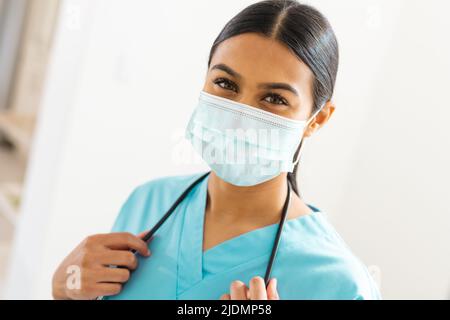 Portrait einer biracial jungen Ärztin, die in der Klinik eine schützende Gesichtsmaske trägt Stockfoto