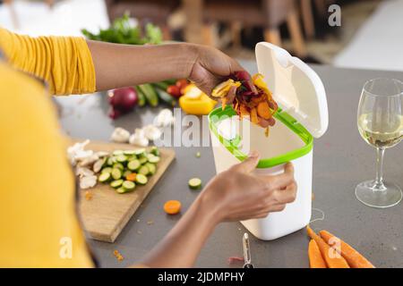 Verkürzte Hände einer afroamerikanischen Frau mittleren Erwachsenen, die Gemüseschalen in Komposteimer in der Küche warf Stockfoto