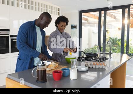 afroamerikanisches Ehepaar mit mittleren Erwachsenen, das in Bademänteln in der Küche frühstücken kann Stockfoto