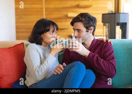 Multirassisches junges Paar, das sich anschaut, während es Kaffee auf dem Sofa im Wohnzimmer hat Stockfoto