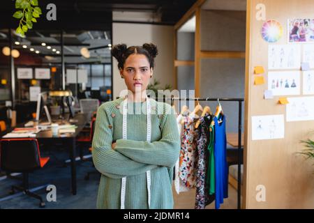 Porträt einer selbstbewussten Biracial-Modedesignerin, die mit gekreuzten Armen im Studio steht Stockfoto