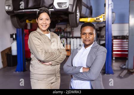 Porträt einer selbstbewussten, multirassischen Ingenieurin mit mittleren Erwachsenen und gekreuzten Armen, die in der Werkstatt stehen Stockfoto