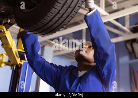 afroamerikanische Mechanikerin mittleren Erwachsenen, die den Autoreifen in der Werkstatt untersucht Stockfoto