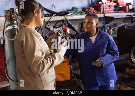 Asiatische Mechanikerin für mittlere Erwachsene, die in einem Workshop mit einer afroamerikanischen Kollegin über ihre Arbeit diskutiert Stockfoto